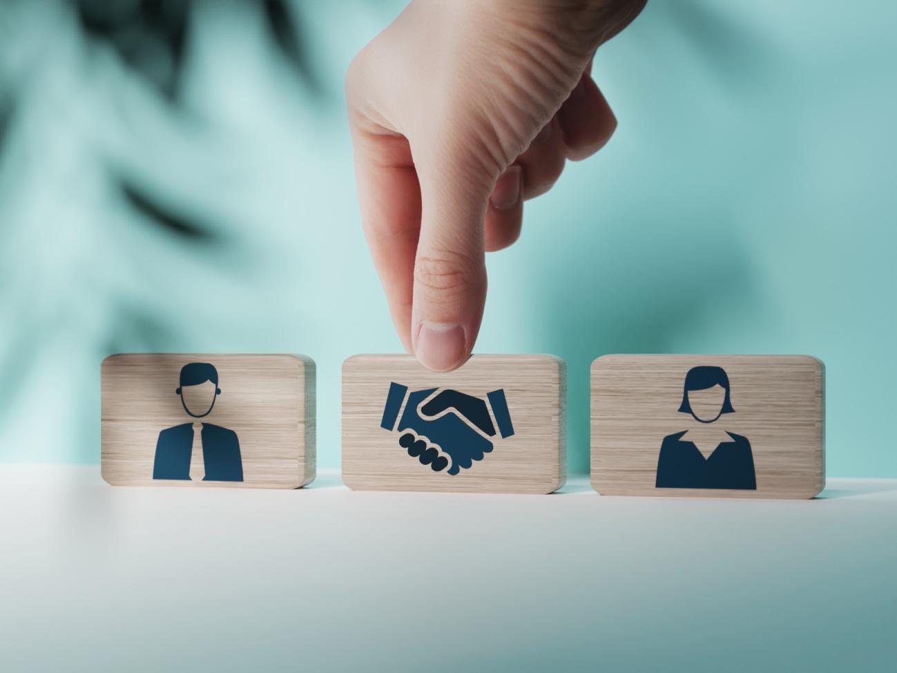 three wooden blocks one with a man one with a woman and one between with shaking hands